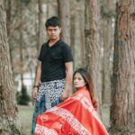 Photo of a Man in a Black Shirt Standing Near a Woman with a Red Fabric