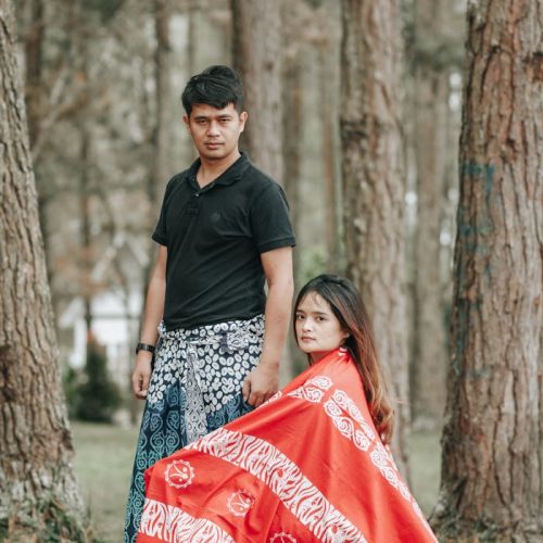 Photo of a Man in a Black Shirt Standing Near a Woman with a Red Fabric